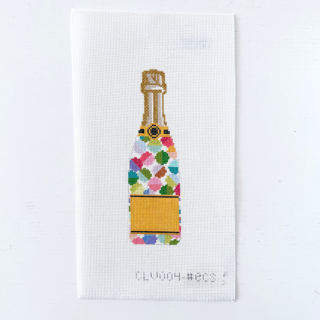 needlepoint design of a colorful champagne bottle on white fabric.