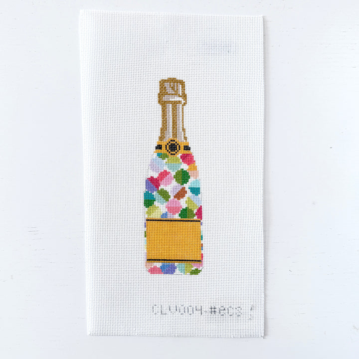 needlepoint design of a colorful champagne bottle on white fabric.